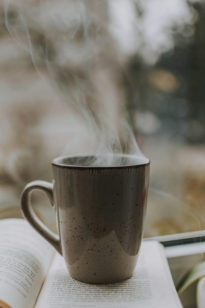 A cozy scene with a steaming coffee mug resting on an open book by the window, perfect for relaxation.
