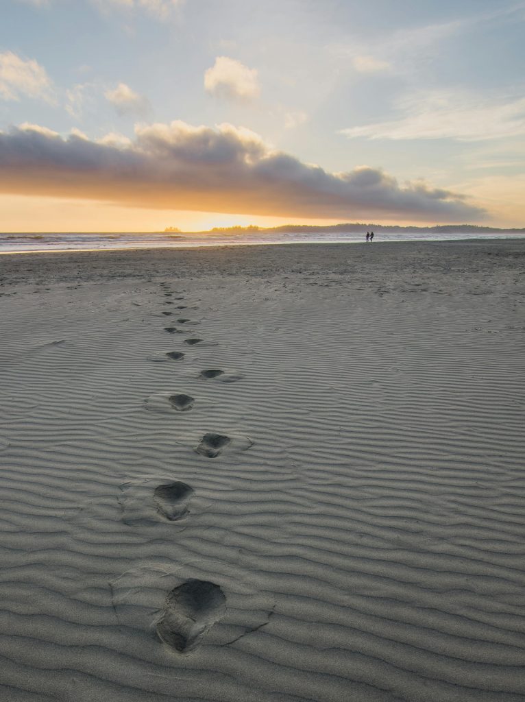 Tranquil beach scene at sunset with footprints leading to the horizon.